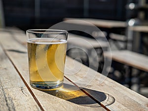 Short glass of blond beer sitting on outdoor table during summer day`