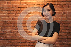 A short haired asian woman wearing a black shirt is smiling on brick wall