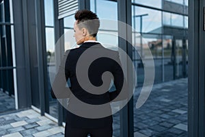 Short-haired business lady in a jacket stands with her back and walks to the front door of a modern office building