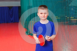 Short - haired eight-year-old boy holds a racket and a table tennis ball. smiling athlete baby
