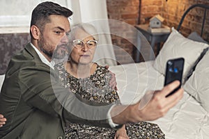 short-haired grandmother and her bearded grandson making duck face and taking a selfie during Grandmother& x27;s Day