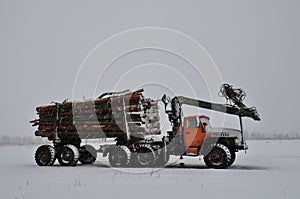 Short log truck in the snow, timber truck, loading logs in winter. manipulator loader logs