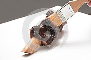 Short rib is coated with flavored glaze using a brush on a white board, preparation for a tasty barbeque, cooking concept, copy