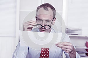 Short sighted at work - balding businessman looking through glasses at document photo