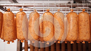 Short smoked sausages hanging on ropes at manufactury.