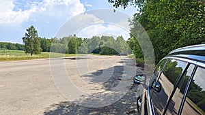 A short stop during a summer road trip. The car is parked in a parking lot near a paved highway with a puddle next to a grassy mea