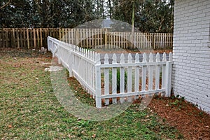 Short white picket fence surrounding a backyard to the paved driveway