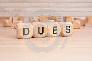 short word english text DUES on a wooden cubes with wooden background photo