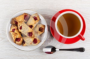 Shortbread cookies with jam in saucer, red cup with tea, teaspoon on table. Top view