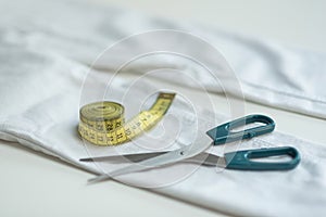 Shortening jeans. White jeans, Measuring tape, scissors on table. Jeans cutting.