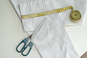 Shortening jeans. White jeans, Measuring tape, scissors on table. Jeans cutting.