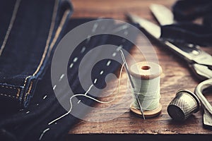Shortening jeans. Spool of  thread, thimble and scissors on table. Jeans cutting