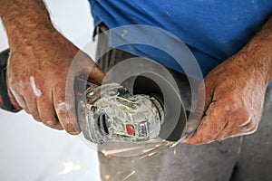 Shortening screw with old rotary cutter, sparks flying as metal is cut, closeup detail on man unprotected hands holding the piece