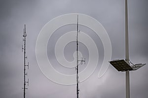 Shortwave antennas and outdoor LED panel light on big masts against gray clouds