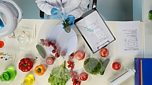 In the shot above, a scientist is sitting. Around her on the table are vegetables and laboratory supplies. She is