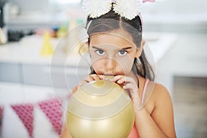 It feels like Im doing all the work. Shot of an adorable little girl blowing up a balloon at her birthday party.