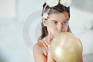 I want to see how big it gets. Shot of an adorable little girl blowing up a balloon at her birthday party.