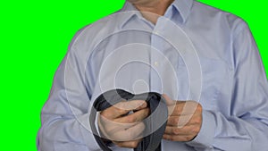 Shot of a adult caucasian man tying his tie in front of camera. Man knots tie. Blue shirt, close up shot. Green screen