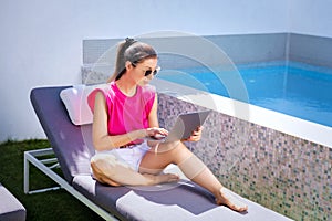 Shot of an attractive woman using laptop while relaxing on sundeck by the pool
