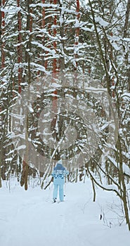 Shot from the back of a retired woman in a blue suit, who walks on classic skis