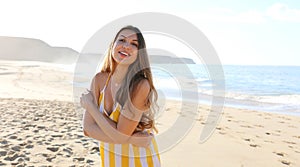 Shot of a beautiful brazilian woman hugging herself while standing on a beach in summer dress