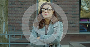 Shot of the beautiful businesswoman in the glasses with hands crossed in front near the big office biuilding. Portrait photo