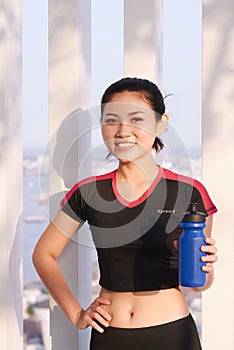 Shot of beautiful female runner holding water bottle. Fitness woman taking a break after running workout outdoor