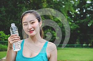 Shot of beautiful female runner standing outdoors holding water bottle. Fitness woman taking a break after running workout