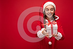 Shot of beautiful happy smiling brunette girl isolated over red background wall wearing new year santa claus outfit