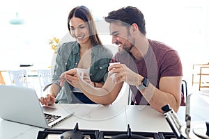 Beautiful lovely young couple using their laptop and having breakfast in the kitchen at home