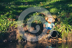 Shot of a beautiful soft toy monkey sitting on the grass near the water in the daytime