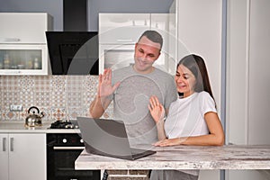 A shot of beautiful young caucasian couple standing at kitchen table in front of open laptop computer, looking at screen and