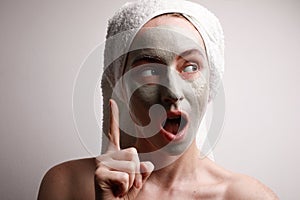 Shot of beautiful young woman look aside with finger up gesture clay facial mask, wrap towel on head. Beauty concept.