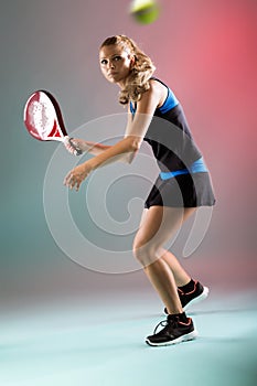 Beautiful young woman playing padel indoor over multicolored background. photo