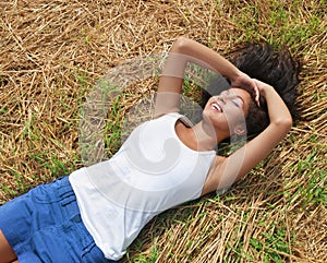 All I need is me. Shot of a beautiful young woman relaxing on a bed of grass outdoors.