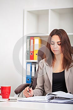 Shot of beautiful young woman sitting at her work desk going through some documents. European business woman working in modern