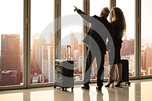 Shot from behind of business travelers standing inside the room which have city view while the man pointing out toward at the