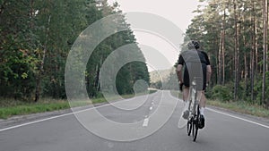 Shot from behind of a man speeding on a road bike in the woods, wearing a helmet