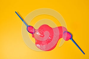 Shot of a blue plastic spoon with pink sticky slime on yellow background. Minimalism in photography, concept creative picture