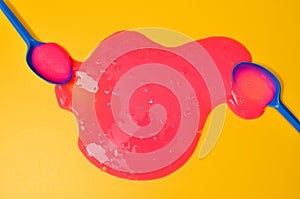 Shot of a blue plastic spoon with pink sticky slime on yellow background. Minimalism in photography, concept creative picture
