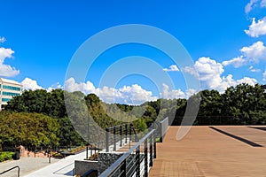 A shot of a brown deck with buildings surrounded by lush green trees with a gorgeous blue sky with clouds at Lenox Park