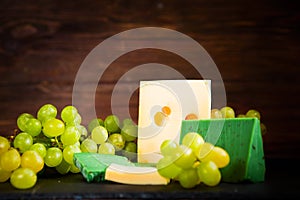 Shot of cheese and green grapes on black slate cheeseboard on wooden table