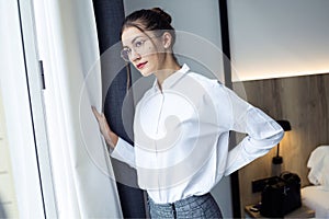 Confident young businesswoman looking sideways standing near the window at hotel room