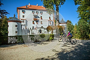 Shot of a couple cycling in front of the Grad SneÅ¾nik castle in Slovenia