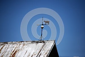 Shot of a cow weathervane on a roof showing west with clear blue sky in the background