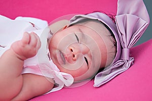 A shot of a cute baby girl with purple headband while sleeping and playing on the pink chair / Focus at infant girl