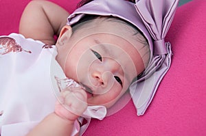 A shot of a cute baby girl with purple headband while sleeping and playing on the pink chair / Focus at infant girl
