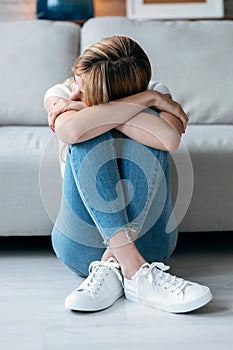 Depresive young woman thinking about her problems while sitting on the floor in the living room at home