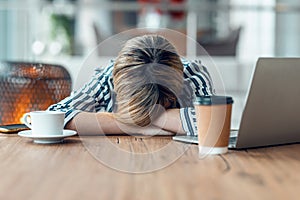 Exhausted young business woman who has fallen asleep while working wirh laptop in living room at home