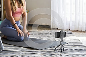 Shot of fitness woman sitting on yoga mat and using mobile phone. Fit young woman using cellphone while doing exercise at home.